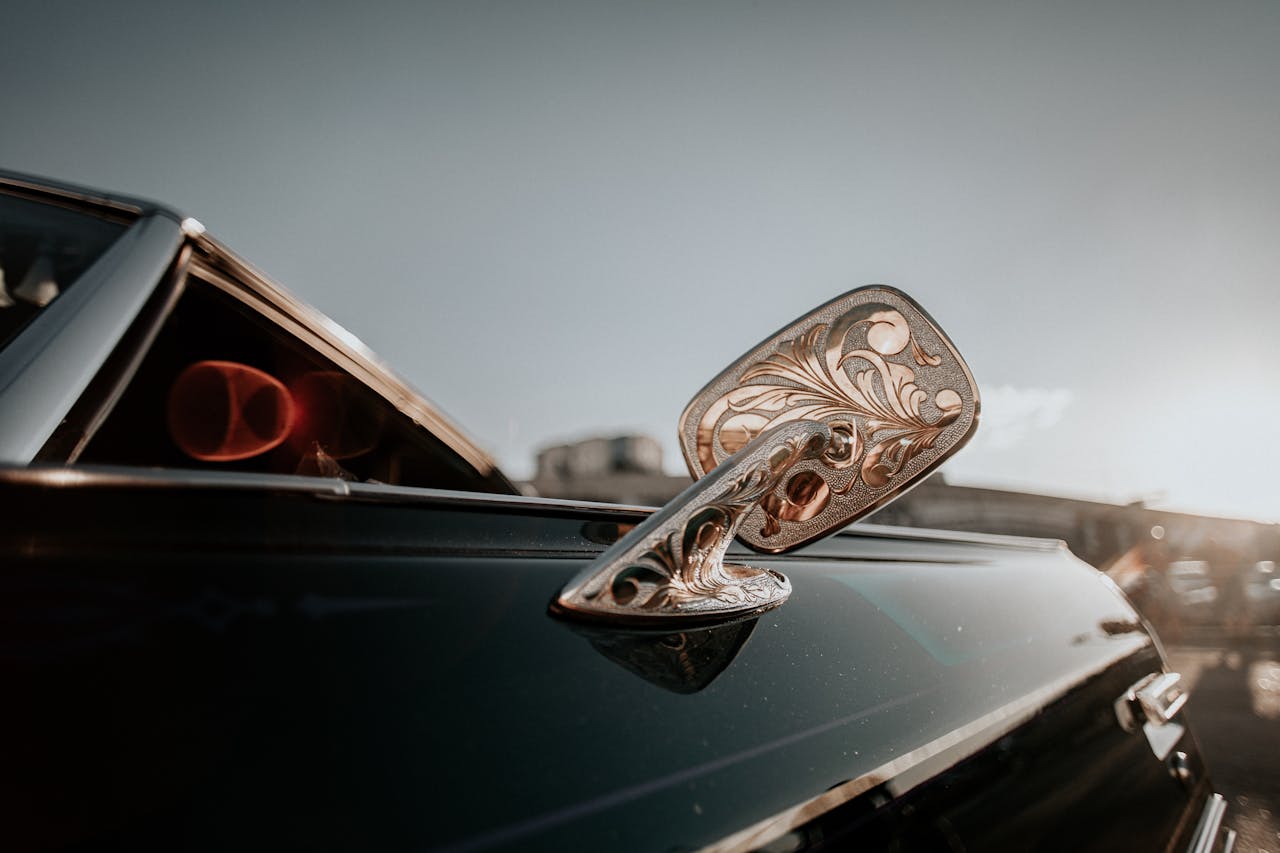 Intricate floral design on car mirror with sleek vehicle, captured in warm sunlight.
