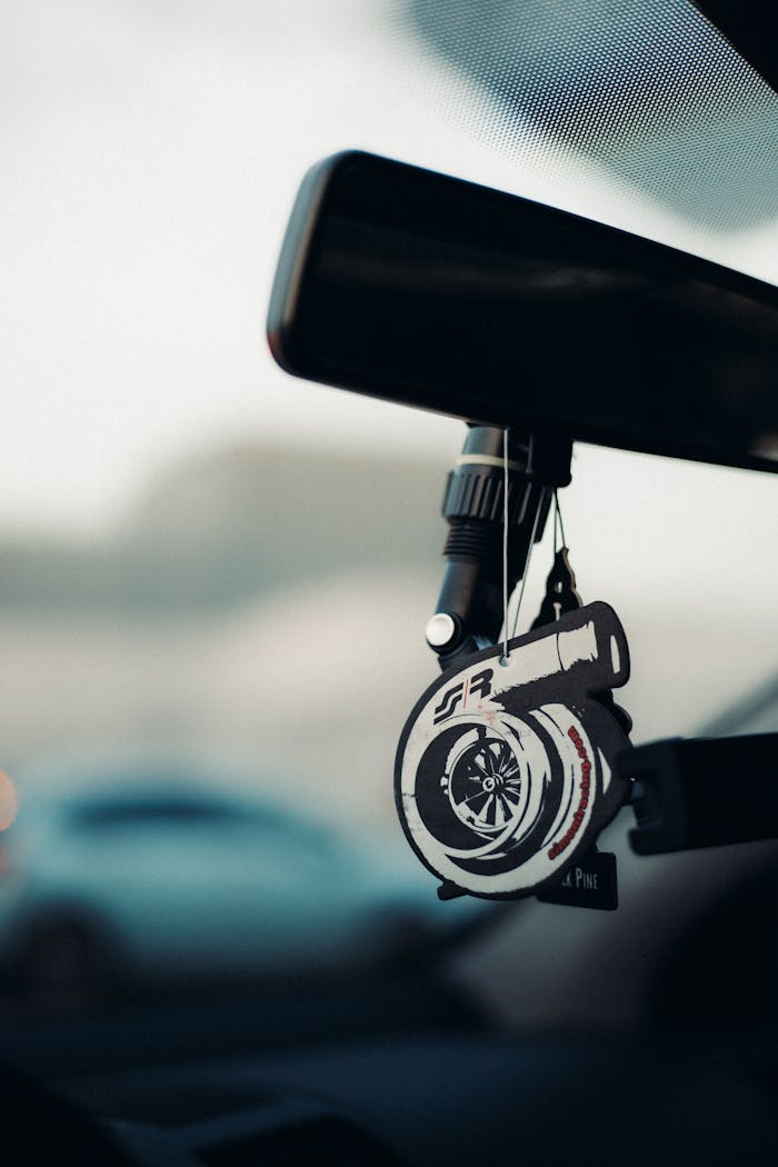 Close-up of a turbo-shaped car air freshener hanging on a rearview mirror in daylight.