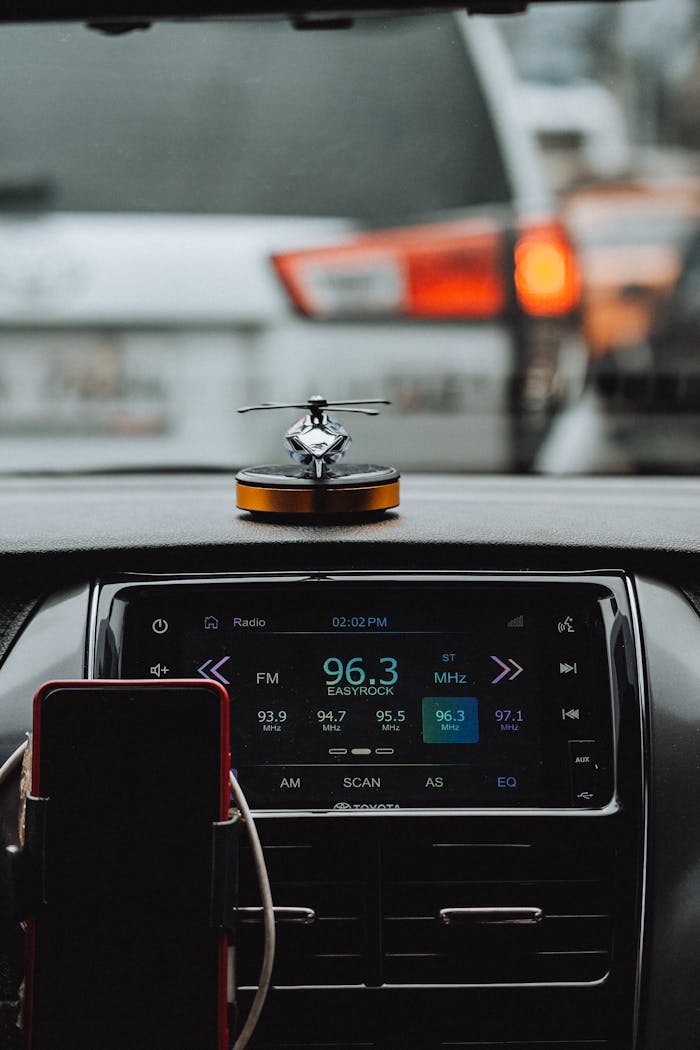 Close-up of a car dashboard with an FM radio tuner, showing specific radio stations and a small helicopter ornament.